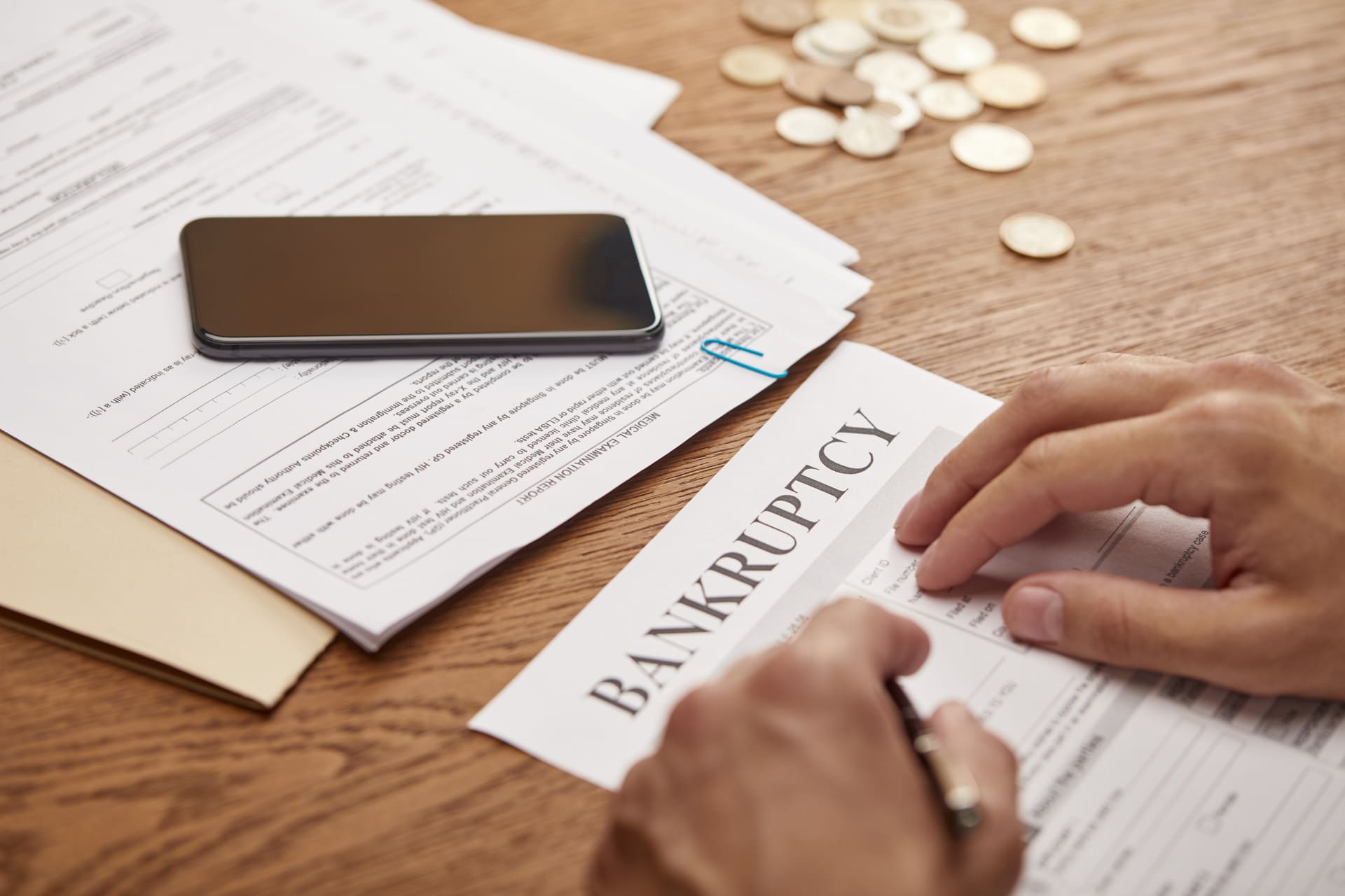 Person filling out a bankruptcy form with papers and coins on the desk