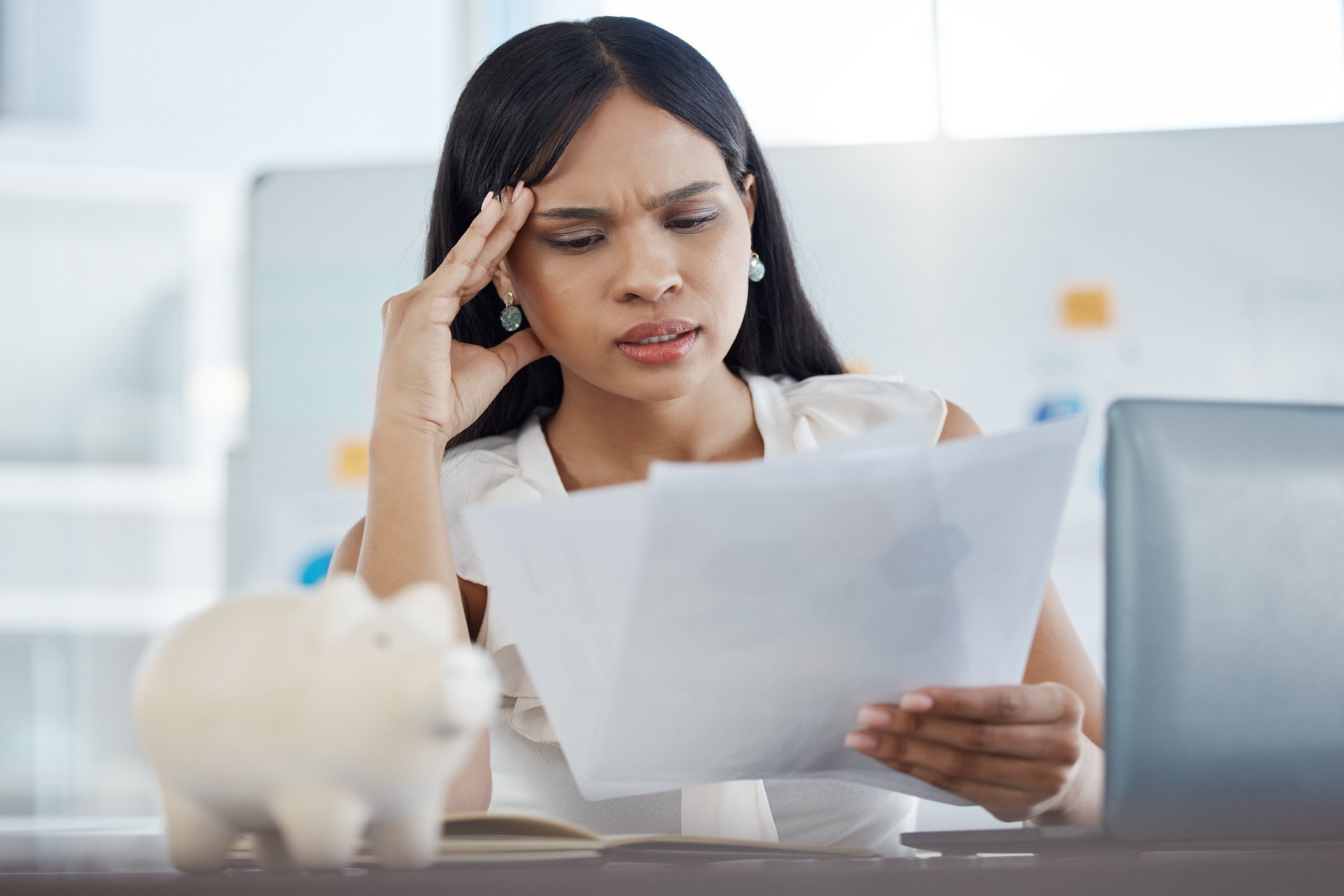 Stressed woman holding her head while reviewing paperwork in office