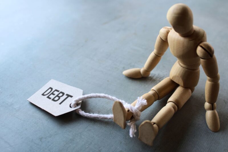 debt concept with wooden figure chained to "debt"