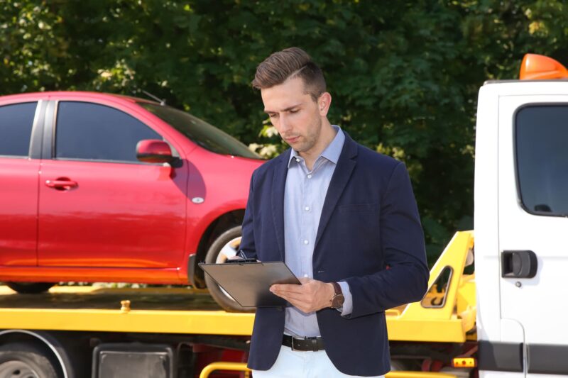 man-inspecting-red-car-on-tow-truck-bed